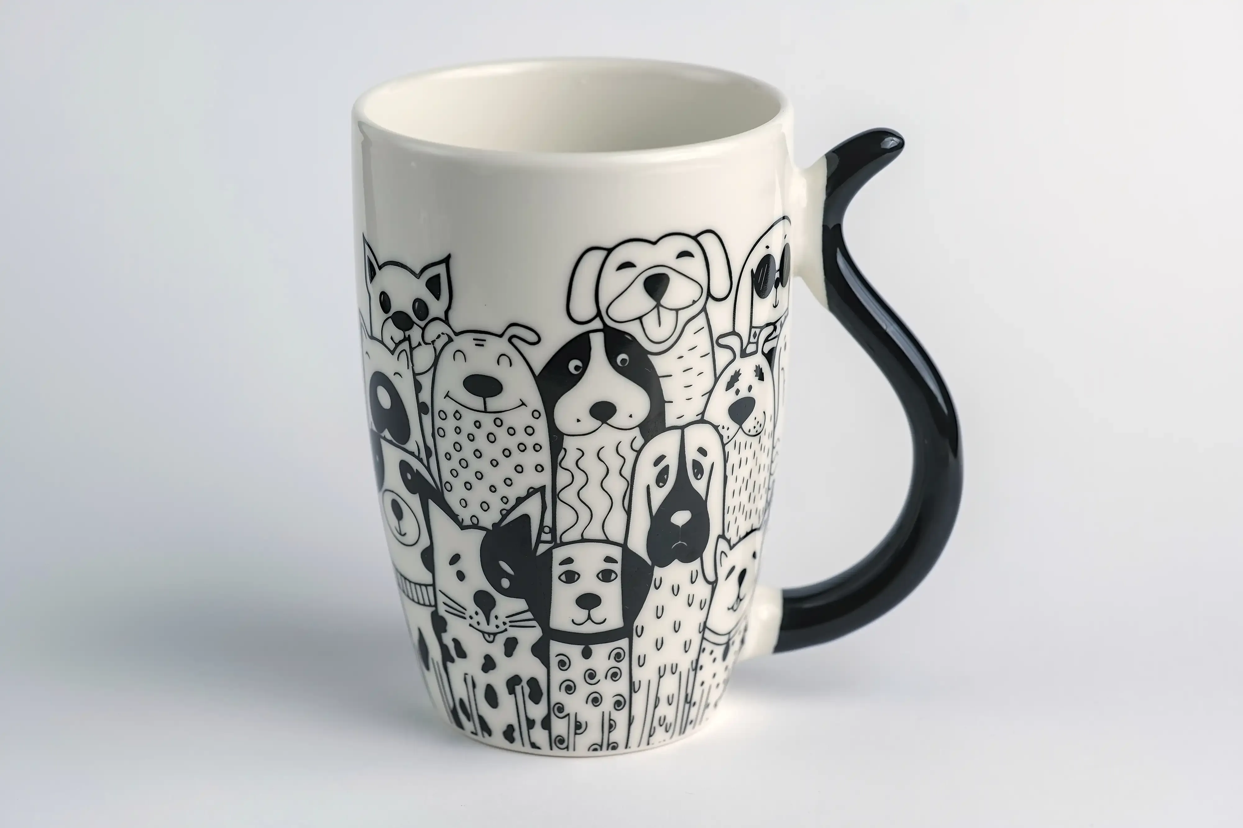 Fotografia de produto de uma caneca branca com uma ilustração de diversos cães em toda a volta. A pega tem a forma de uma cauda de cão a preto.